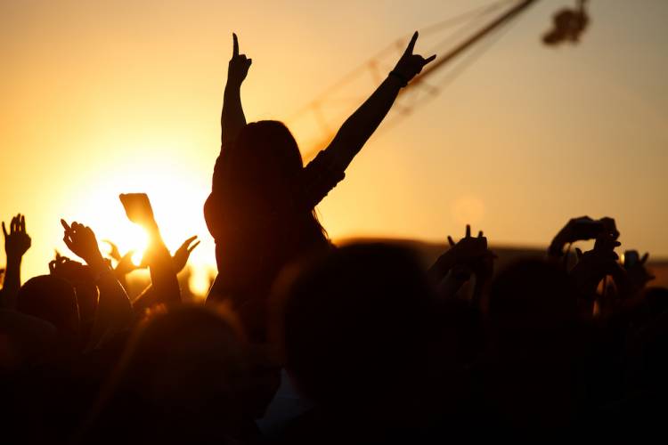 concert audience with girl on someone's shoulders at sunset